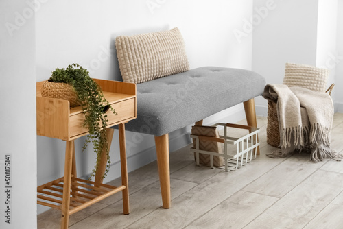 Foto Soft bench with baskets and table near light wall