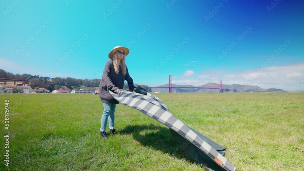 Cheerful female tourist enjoying sunny day with Golden Gate Bridge in the background. Beautiful lady preparing for the outdoor picnic in lush lawn. High quality 4k footage Cheerful female tourist enjoying sunny day with Golden Gate Bridge in the background. Beautiful lady preparing for the outdoor picnic in lush lawn. High quality 4k footage