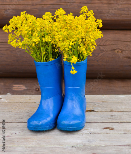 Children's blue rubber boots with yellow flowers are standing on a wooden background
