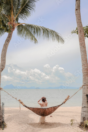 Women in white dress sitting on Wood Swings on palm tree of beach in summer vacation.
