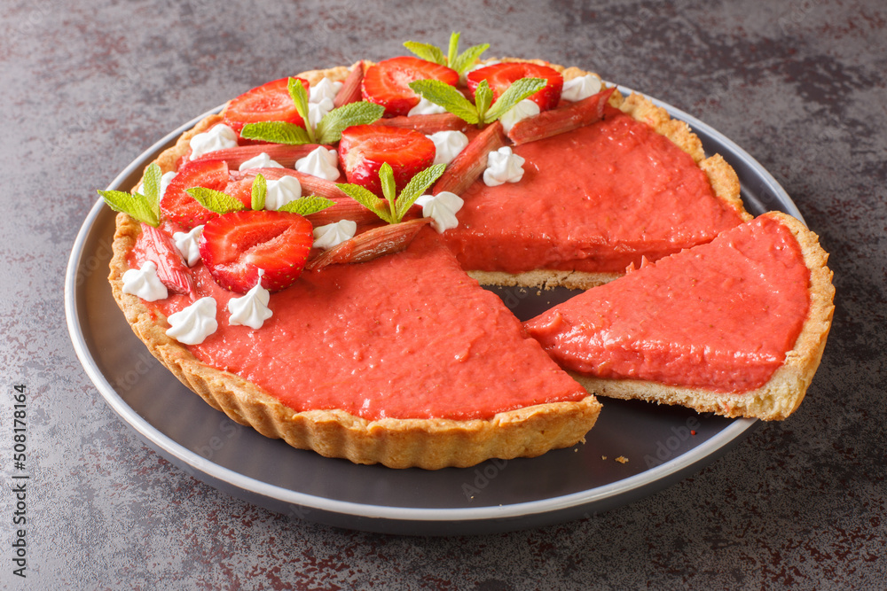 Sliced strawberry and rhubarb tart decorated with mint and whipped cream close-up on a plate on the table. Horizontal Sliced strawberry and rhubarb tart decorated with mint and whipped cream close-up on a plate on the table. Horizontal