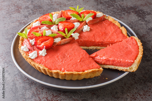 Sliced strawberry and rhubarb tart decorated with mint and whipped cream close-up on a plate on the table. Horizontal