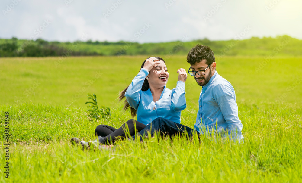 A couple in love sitting in the field, Romantic couple sitting on the grass outdoors, Smiling teenage couple sitting on the grass on a sunny day A couple in love sitting in the field, Romantic couple sitting on the grass outdoors, Smiling teenage couple sitting on the grass on a sunny day