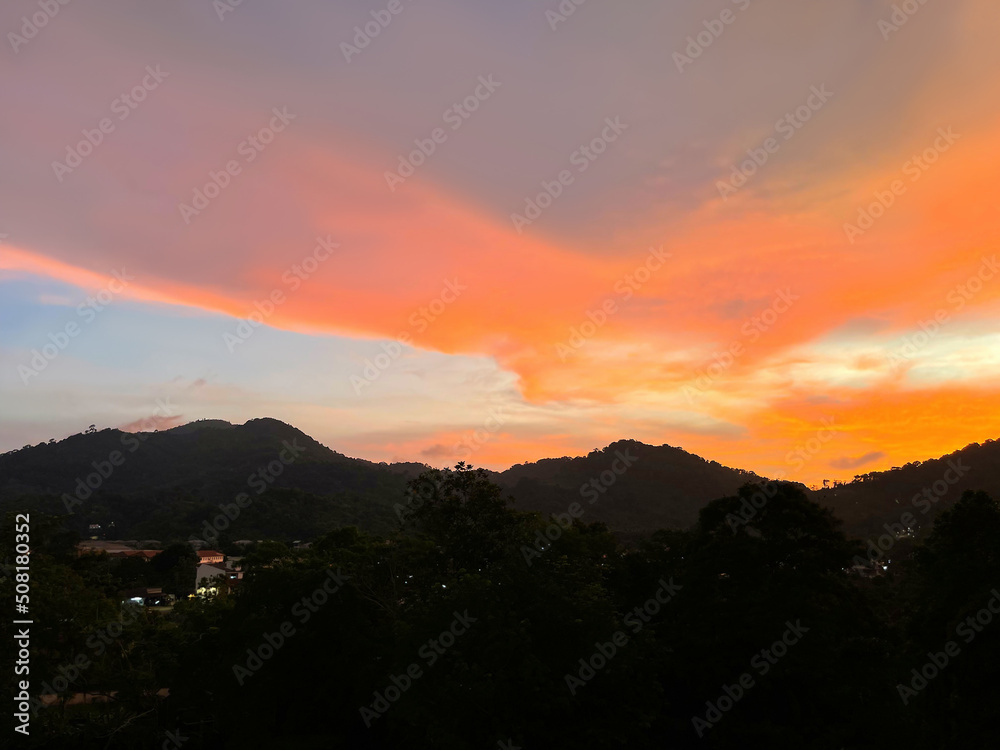Fiery red sunset over mountains and valley. Amazing skies. Multi-colored cloud of a beautiful shape in the night sky. Magnificent panoramic view. Beauty of nature. City lights in the distance. Twiligh