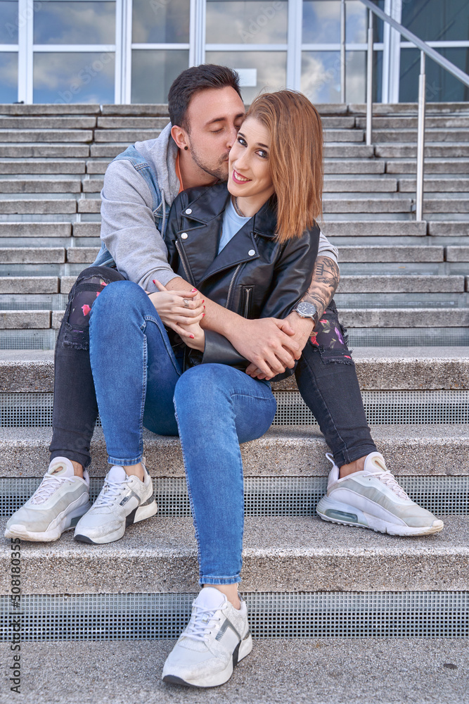 Man hugging and kissing his girlfriend while sitting on the stairs outdoors. Relationship and love concept. Man hugging and kissing his girlfriend while sitting on the stairs outdoors. Relationship and love concept.