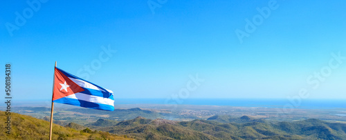 Panorama shot of Cuban flag waving on a pole with nature landscape of Cuba in background. photo