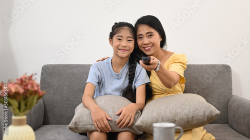 Mother and daughter sitting on sofa and watching tv. Family, children, love and happy people concept