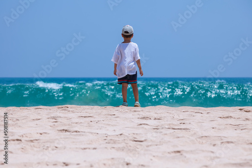 Obraz na płótnie A little boy looks into the blue endless ocean on a tropical beach w salonie