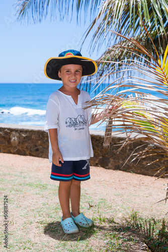 Little boy on a tropical beach next to palm trees against the backdrop of a blue ocean