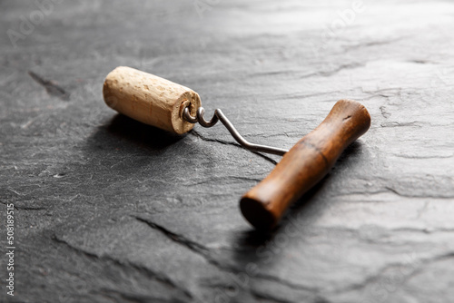 Vintage wine corkscrew in a cork on a black slate background.
