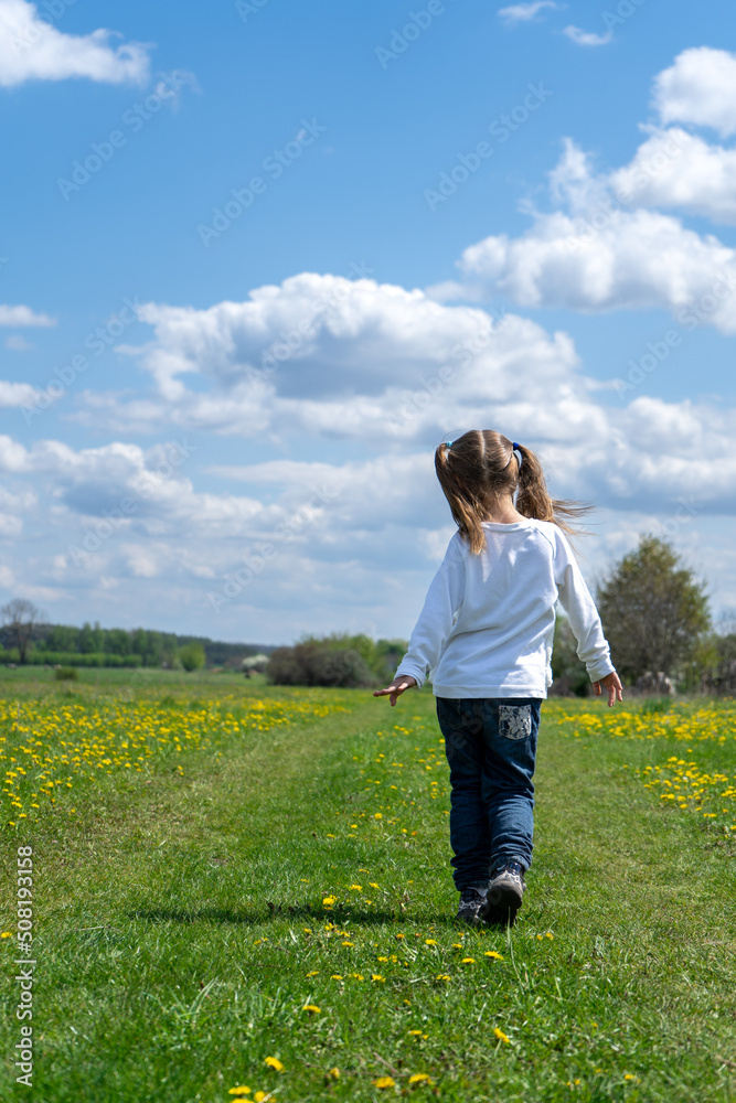 Little girl walks in a beautiful spring field 