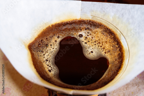 The coffee is brewed in a Chemex filter coffee maker. Coffee is filled with hot water in a white paper filter. photo