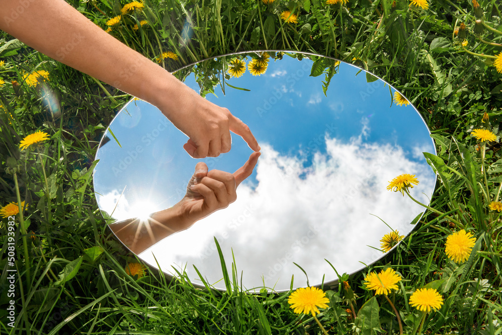 nature concept - hand touching sky reflection in round mirror on summer field - obrazy, fototapety, plakaty 