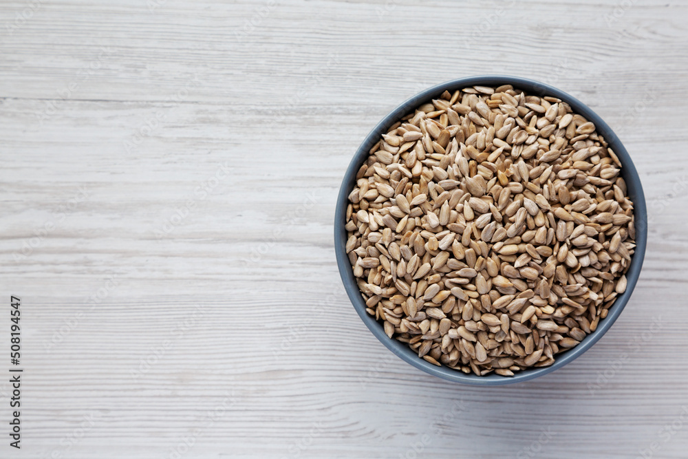 Raw Organic Sunflower Seed Kernels in a Blue Bowl on a white wooden background, top view. Flat lay, overhead, from above. Space for text. Raw Organic Sunflower Seed Kernels in a Blue Bowl on a white wooden background, top view. Flat lay, overhead, from above. Space for text.