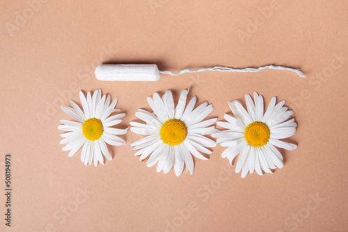 feminine tampon and bloom chamomile flower lie flat lay on brown pastel background. copy space
