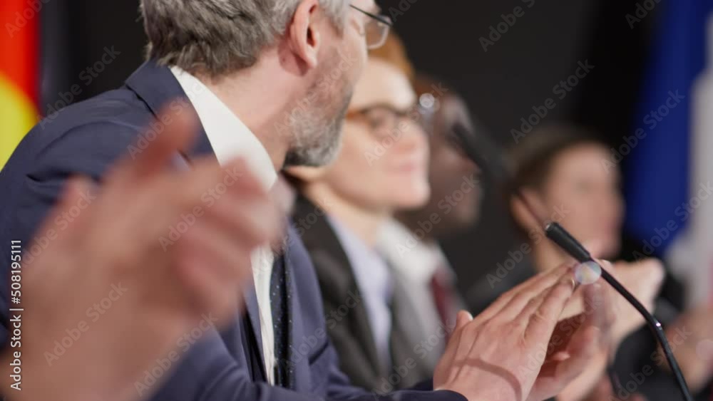 Tilt up selective focus shot of middle aged political leader applauding and smiling during international press conference