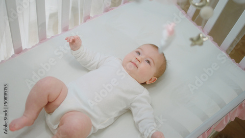 Childhood concept cute baby girl in her baby cot moving from her legs and hands while looking up at the cot toys