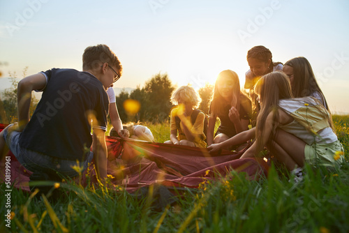 Foto Back view of group of kids setting up red tent in woods at sunset