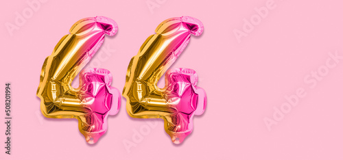 Rainbow foil balloon number, digit forty four on a pink background. Birthday greeting card with inscription 44. Top view. Numerical digit. Celebration event, template. Banner photo
