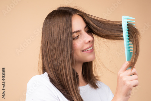 Close up portrait of happy beautiful girl with shiny hair with comb. Attractive smiling woman brushing hair.