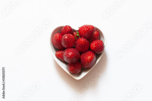 Strawberries, top view of sweet and delicious red strawberries in heart shaped bowl, isolated on white background, selective focus.