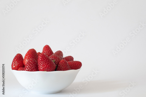 Strawberries, natural and sweet ripe strawberries in white bowl with copy space on right. Isolated on white background, selective focus.