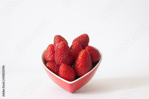 Strawberries, angled view of sweet and delicious red strawberries in heart shaped bowl, isolated on white background, selective focus.