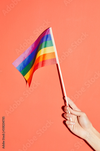 Vibrant shot of female hand holding rainbow flag at pink background as symbol for pride month LGBTQ