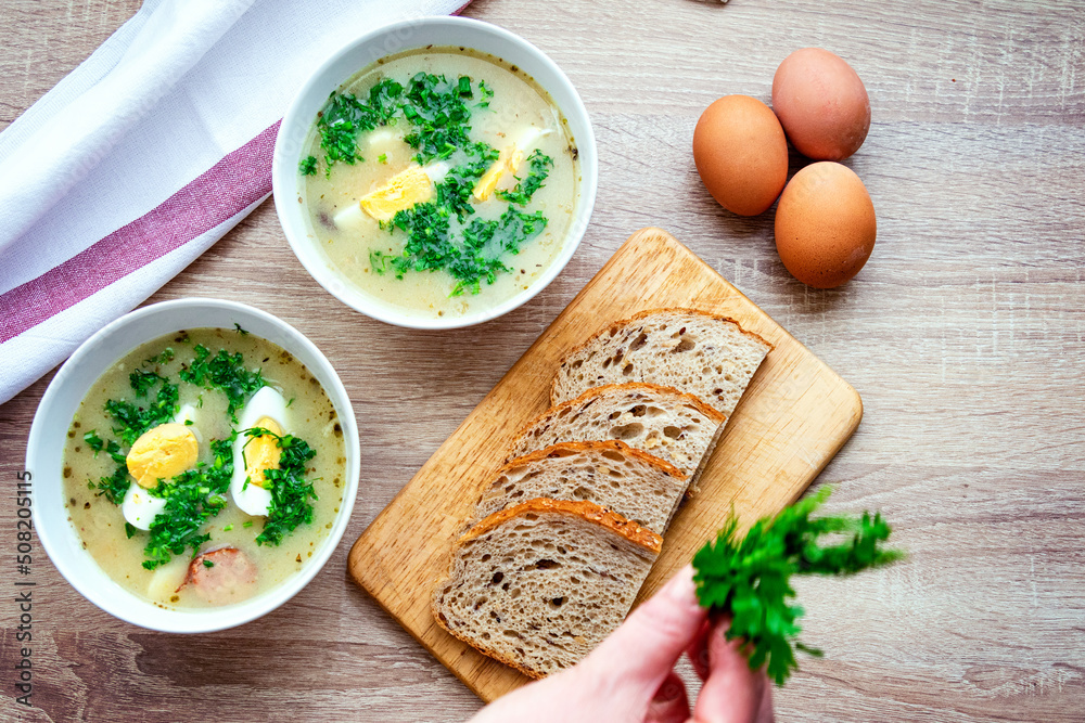 Zurek is a traditional Polish soup. Two bowls of hot soup with egg and sausage, bread and fresh herbs on the table. Zurek is a traditional Polish soup. Two bowls of hot soup with egg and sausage, bread and fresh herbs on the table.