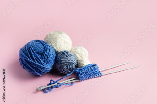 Blue and white knitted wool on a pink background with knitting needles for knitting warm clothes, hobbies
