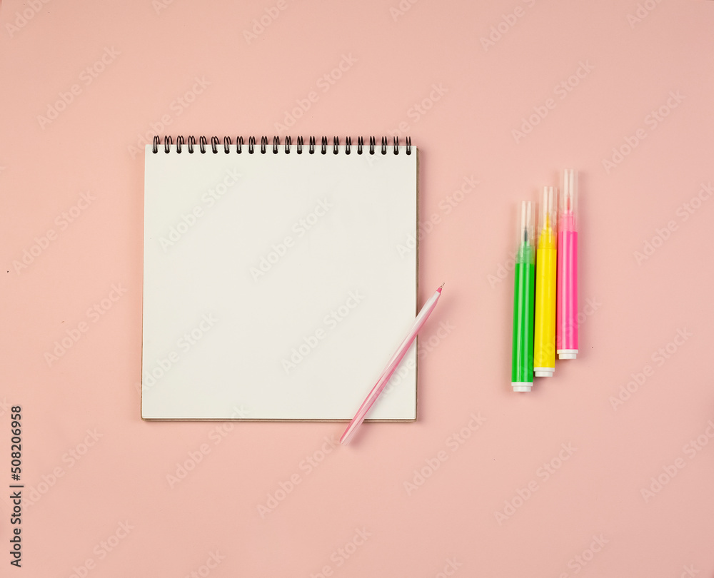 Notepad with white sheets and a pen and markers for writing on a pink background with copy space. Education concept.