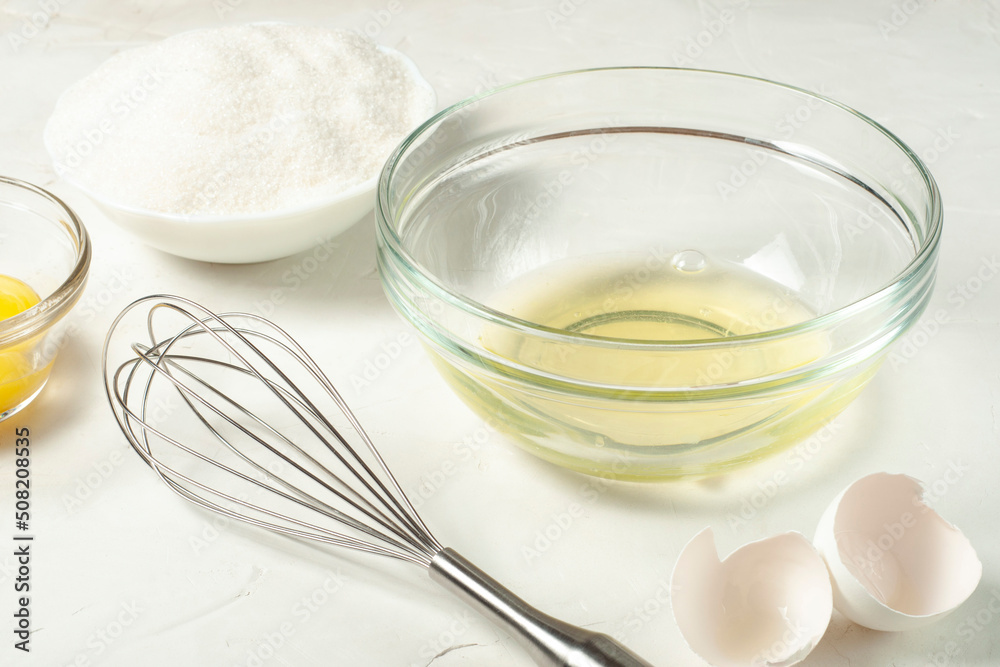 ingredients for the French meringue dessert - egg white, sugar, whisk, eggshell and separated yolk on a gray background close-up. ingredients for the French meringue dessert - egg white, sugar, whisk, eggshell and separated yolk on a gray background close-up.