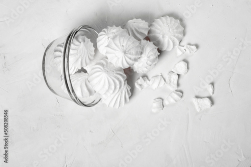 glass vase with a French dessert meringue lies on a gray background. part of the meringue spilled out of the vase onto the table. whole and broken parts of the meringue are visible. fly, copy space.