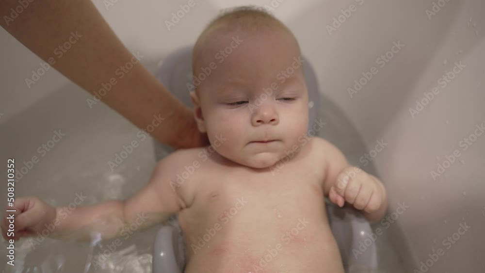 Portrait of an adorable cute baby taking his first bath and smiling. Bathing a newborn in a tub. First days of life. A little boy takes a bath for the first time. Portrait of an adorable cute baby taking his first bath and smiling. Bathing a newborn in a tub. First days of life. A little boy takes a bath for the first time.