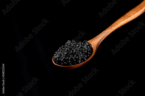 Wooden spoon with black caviar isolated on black background.