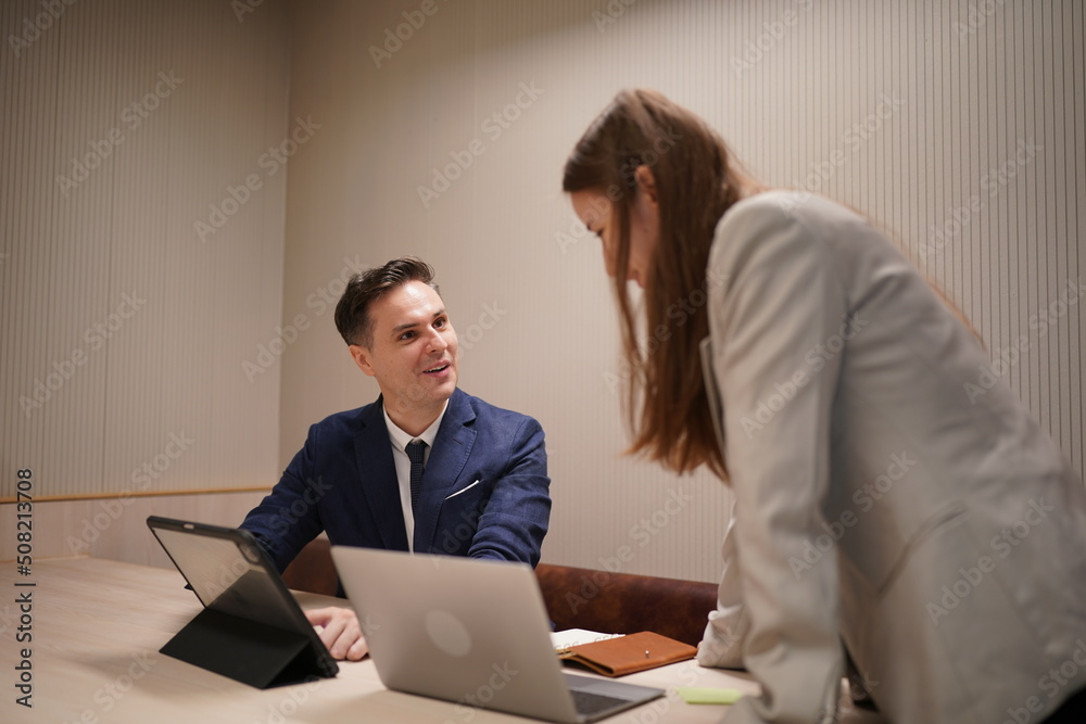 Image of young businessmen and colleague discussing document in laptop and touchpad at meeting Image of young businessmen and colleague discussing document in laptop and touchpad at meeting