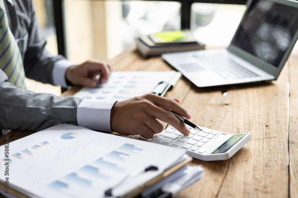 Businessman working on desk office with using a calculator to calculate the finance numbers and calculate about cost to real estate investment and in other, tax system. Finance accounting concept. Businessman working on desk office with using a calculator to calculate the finance numbers and calculate about cost to real estate investment and in other, tax system. Finance accounting concept.