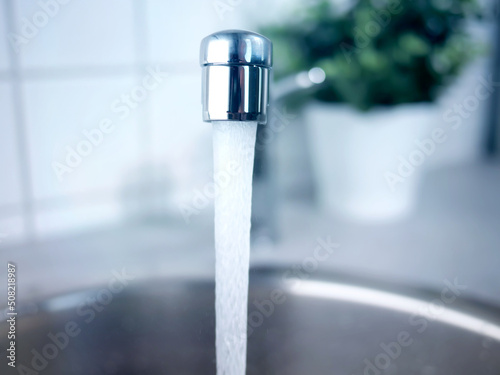 A stream of clean water drink flows from the kitchen faucet into the stainless steel sink. Environment, water pollution and water shortage concept