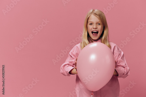 horizontal portrait of a cute, beautiful, happy girl with blond hair hugging a big balloon standing in a pink dress on a pink background with an empty space for an advertising tex © Tatiana