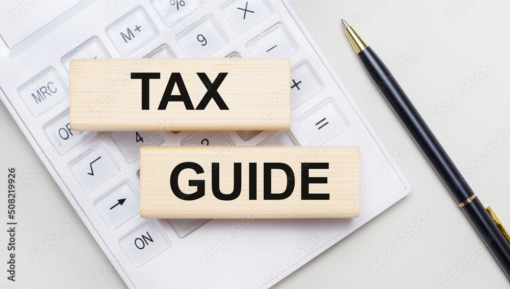 Wooden blocks with the TAX GUIDE Iie on a light background on a white calculator. Nearby is a black handle. Business concept Wooden blocks with the TAX GUIDE Iie on a light background on a white calculator. Nearby is a black handle. Business concept