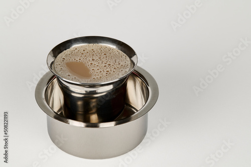 South Indian filter coffee in a steel tumbler and steel dabarah on a white background