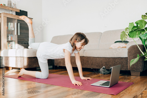 The girl performs sports exercises at home. Online workouts. Mobility of children and a healthy lifestyle