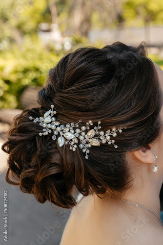 hairstyle of the bride with brown hair, collected in a bun and decorated with a wedding decoration made of metal and stones