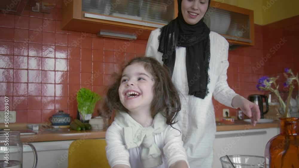 Muslim family spend time in the kitchen. Mom and daughter knead the dough in the kitchen Muslim family spend time in the kitchen. Mom and daughter knead the dough in the kitchen