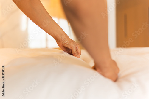 Hand of woman maid making bed in hotel room.