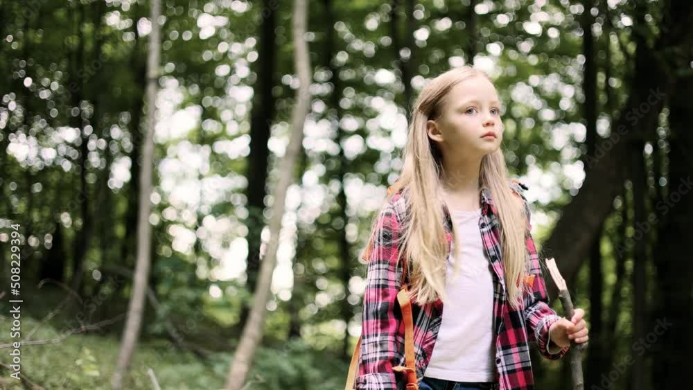 Child with a backpack explores wildlife, a kid stands alone among the trees. Portrait of cute little girl looking at the camera in the forest. Child with a backpack explores wildlife, a kid stands alone among the trees. Portrait of cute little girl looking at the camera in the forest.
