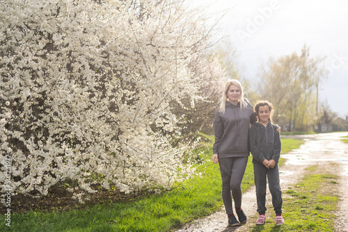 Woman walking with daughter in blooming spring garden exploring flowering tree. Family admires nature. © Angelov