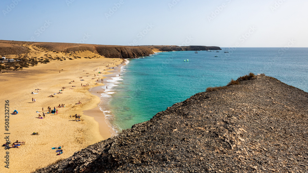 View from hillside over Playa Mujeres, Playa Blanca, Yaiza, Lanzarote, Las Palmas, Islas Canarias, Spain, Europe. Golden sand washed by the clear turquoise waters of the Atlantic Ocean.