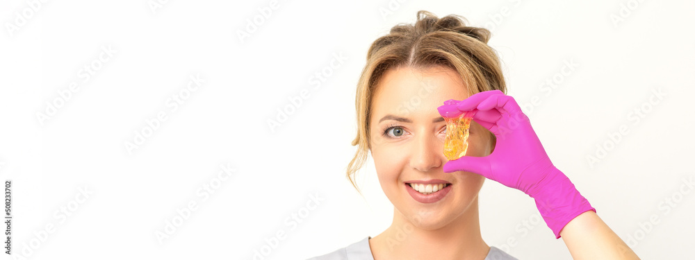 The master of sugar hair removal holds liquid yellow sugar paste, covering her eye with wax for depilation on a white background The master of sugar hair removal holds liquid yellow sugar paste, covering her eye with wax for depilation on a white background