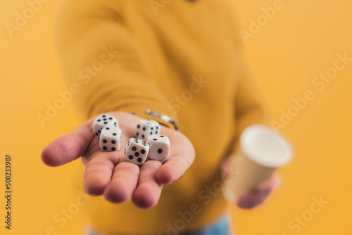 Young European man showing dices in his hand and a cup in another yellow background copy space studio shot . High quality photo photo